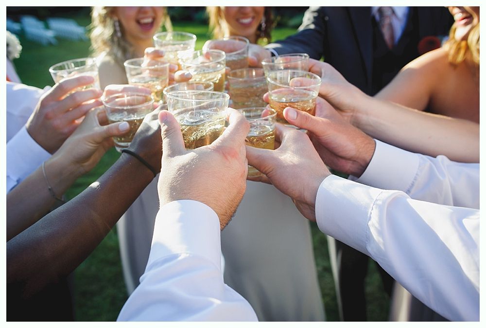 Bride with arms up, making a funny face, groom looking at his hand, cake cutting in background.