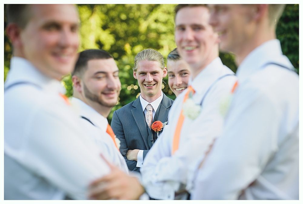 Bride with arms up, making a funny face, groom looking at his hand, cake cutting in background.