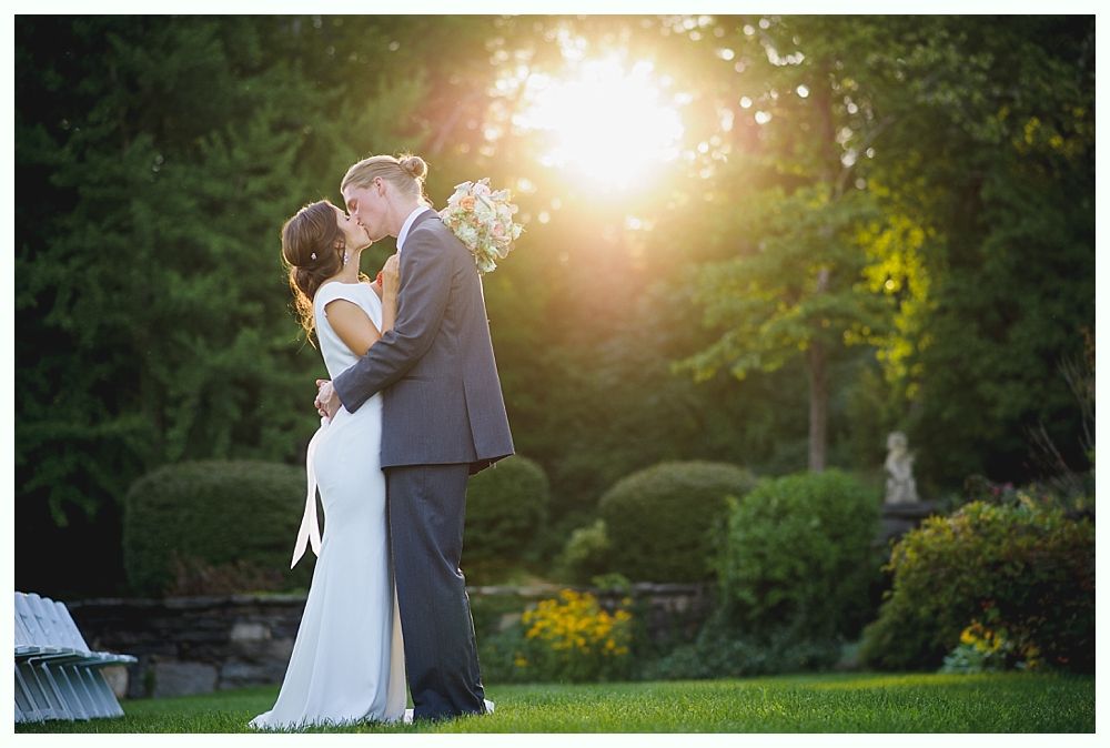 Bride with arms up, making a funny face, groom looking at his hand, cake cutting in background.