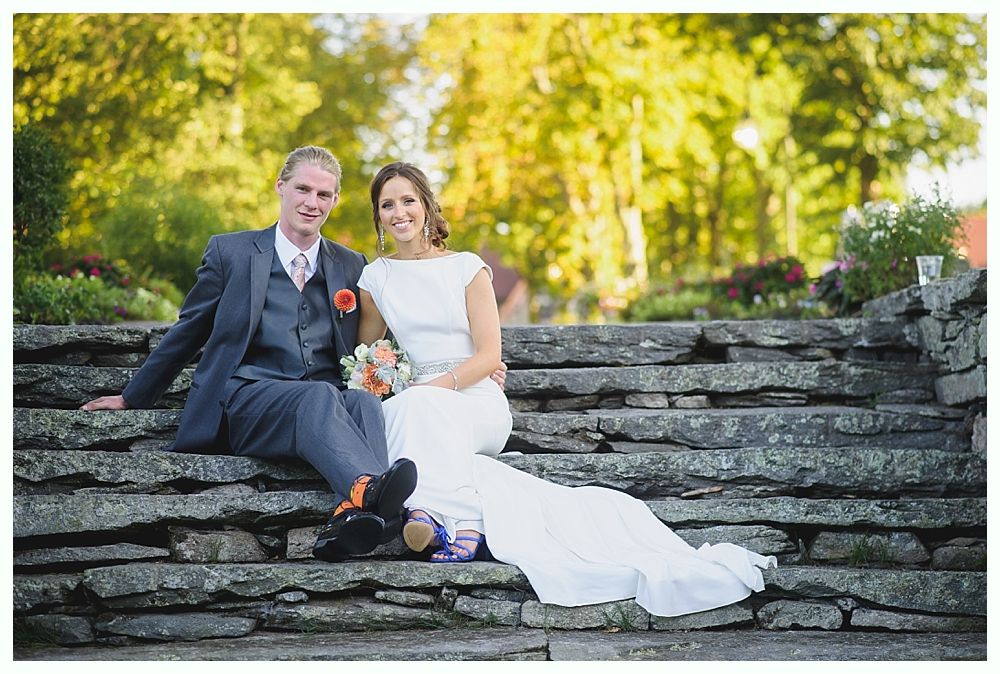 Bride with arms up, making a funny face, groom looking at his hand, cake cutting in background.