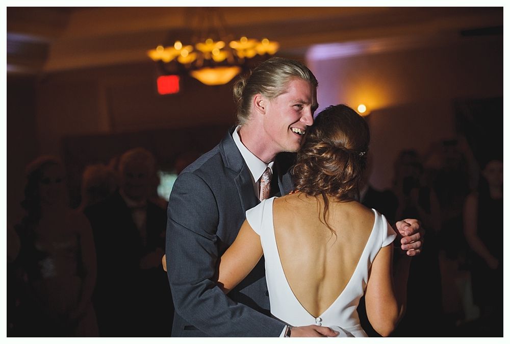 Bride with arms up, making a funny face, groom looking at his hand, cake cutting in background.