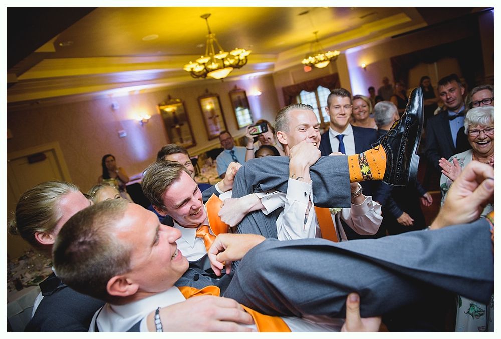 Bride with arms up, making a funny face, groom looking at his hand, cake cutting in background.