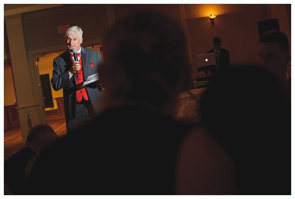 Bride with arms up, making a funny face, groom looking at his hand, cake cutting in background.