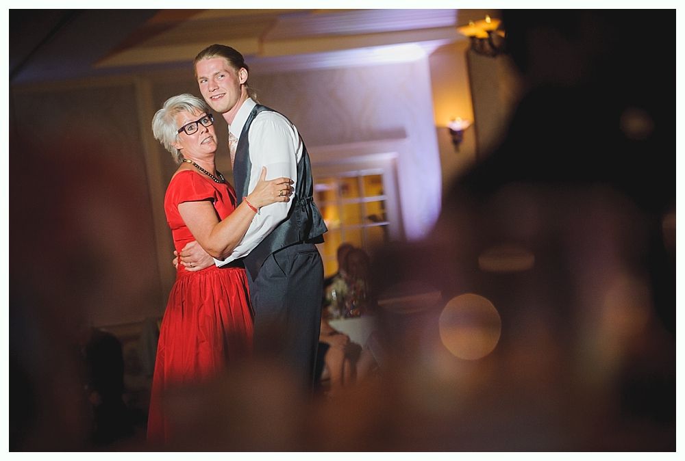 Bride with arms up, making a funny face, groom looking at his hand, cake cutting in background.