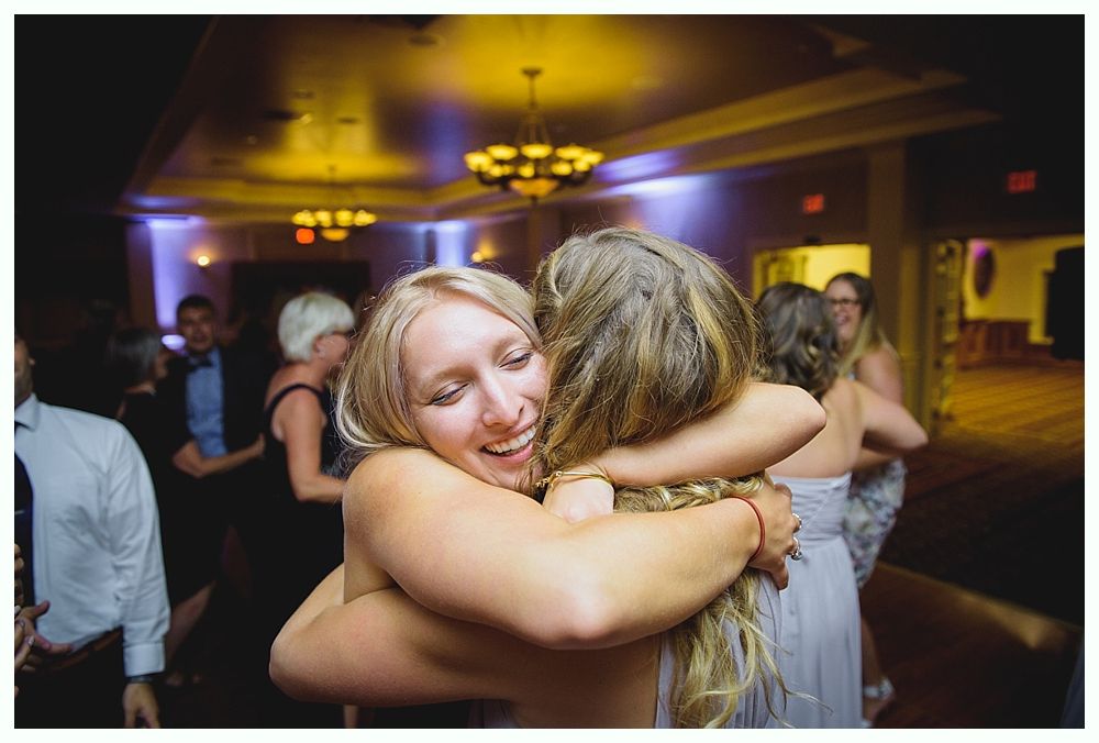 Bride with arms up, making a funny face, groom looking at his hand, cake cutting in background.