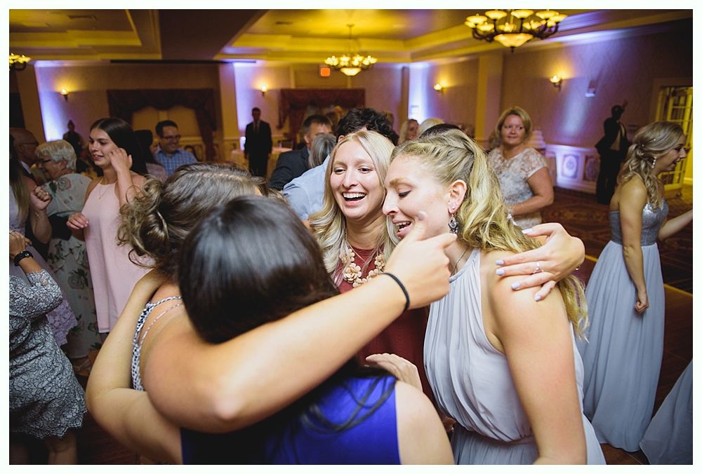 Bride with arms up, making a funny face, groom looking at his hand, cake cutting in background.