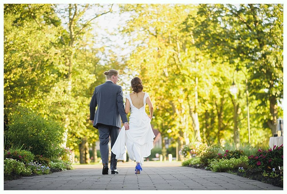 Bride with arms up, making a funny face, groom looking at his hand, cake cutting in background.