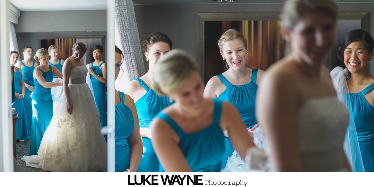 Bride in a white dress, surrounded by bridesmaids in turquoise dresses, smiling in a room.