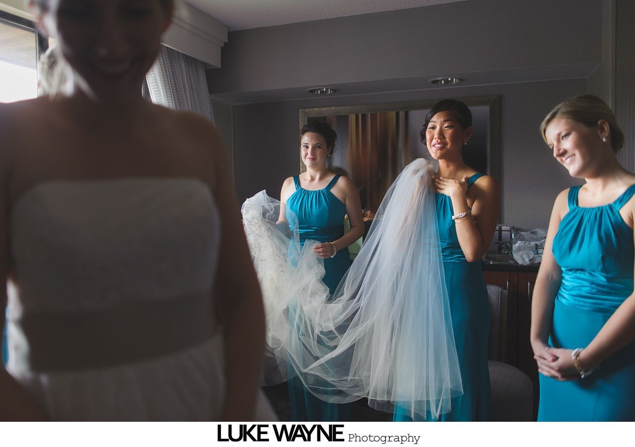 Bride and bridesmaids in teal dresses, with veil; bridesmaids smiling, indoors.