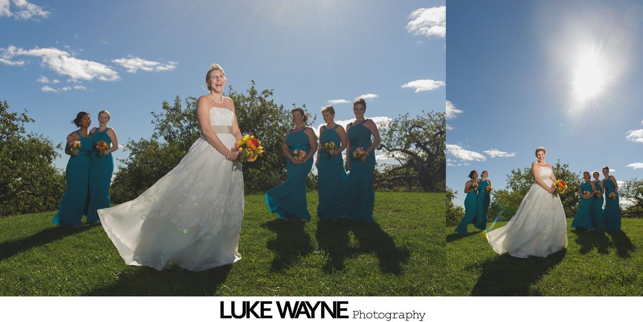 Bride in a white dress with bridesmaids in teal dresses on a grassy field on a sunny day.