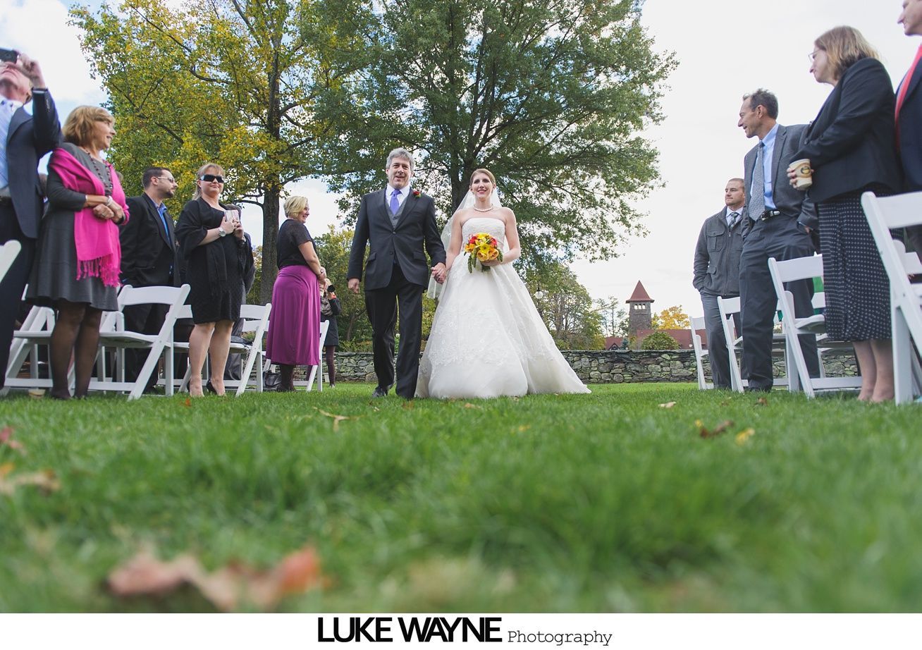 Bride and groom walking down aisle after outdoor wedding ceremony. Guests watch.