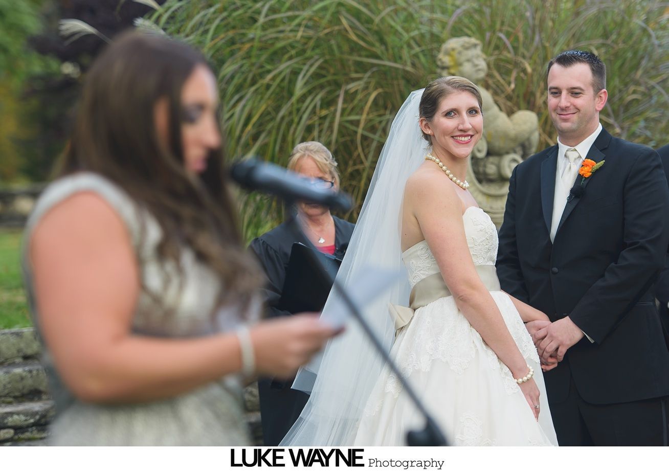 Bride and groom at outdoor wedding ceremony; officiant speaking.