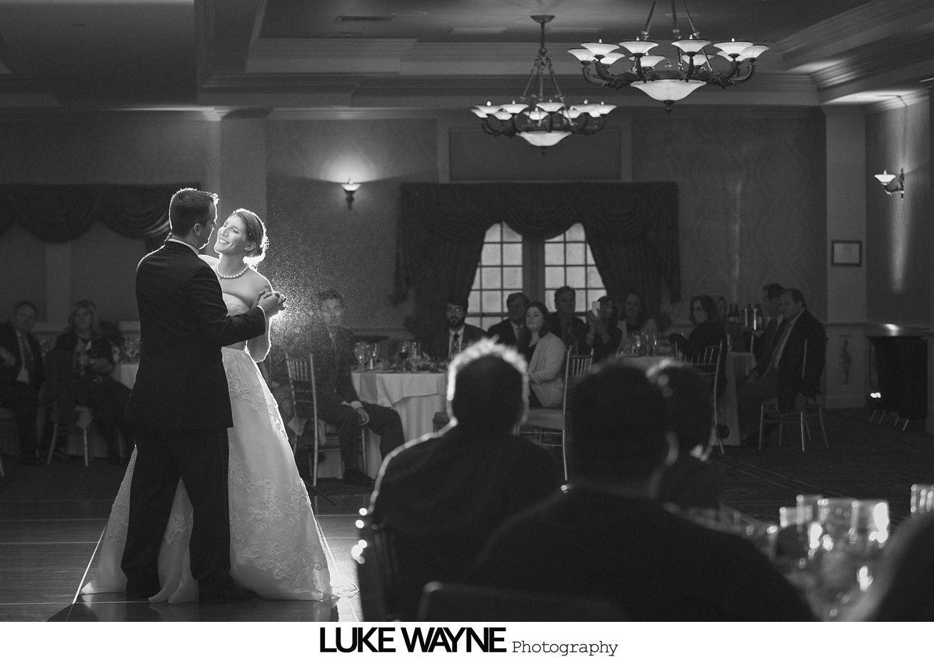Couple dances at a wedding reception; guests watch. Black and white.