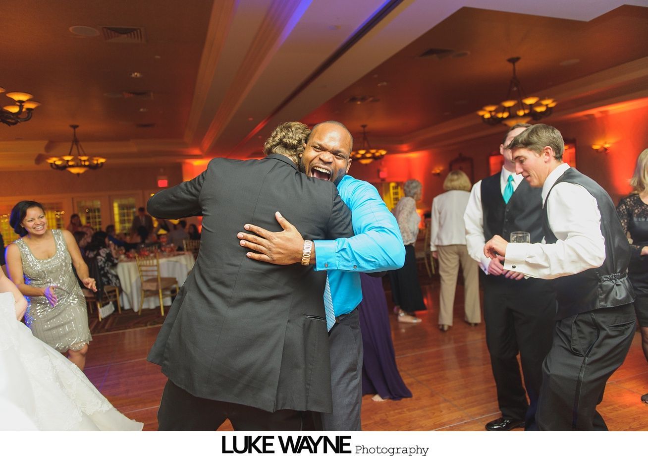 Two men embrace on a dance floor at a wedding reception.