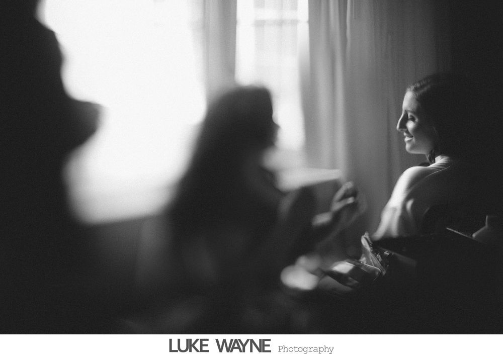 Silhouetted men helping each other with suits in a bright room by a window.