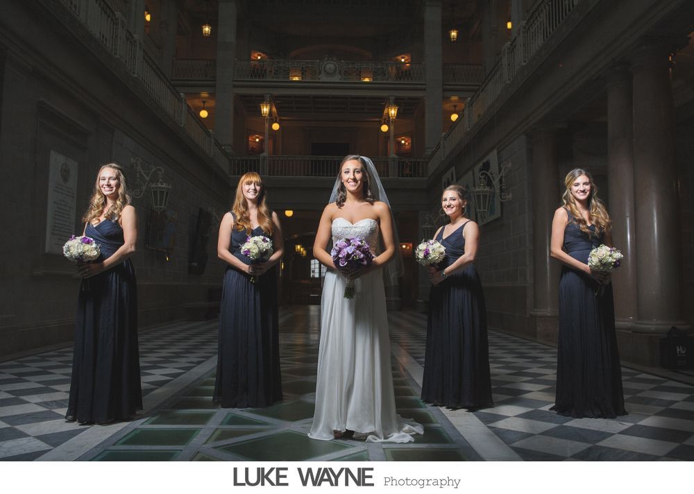 Bride in white dress laughs with bridesmaids in purple gowns.