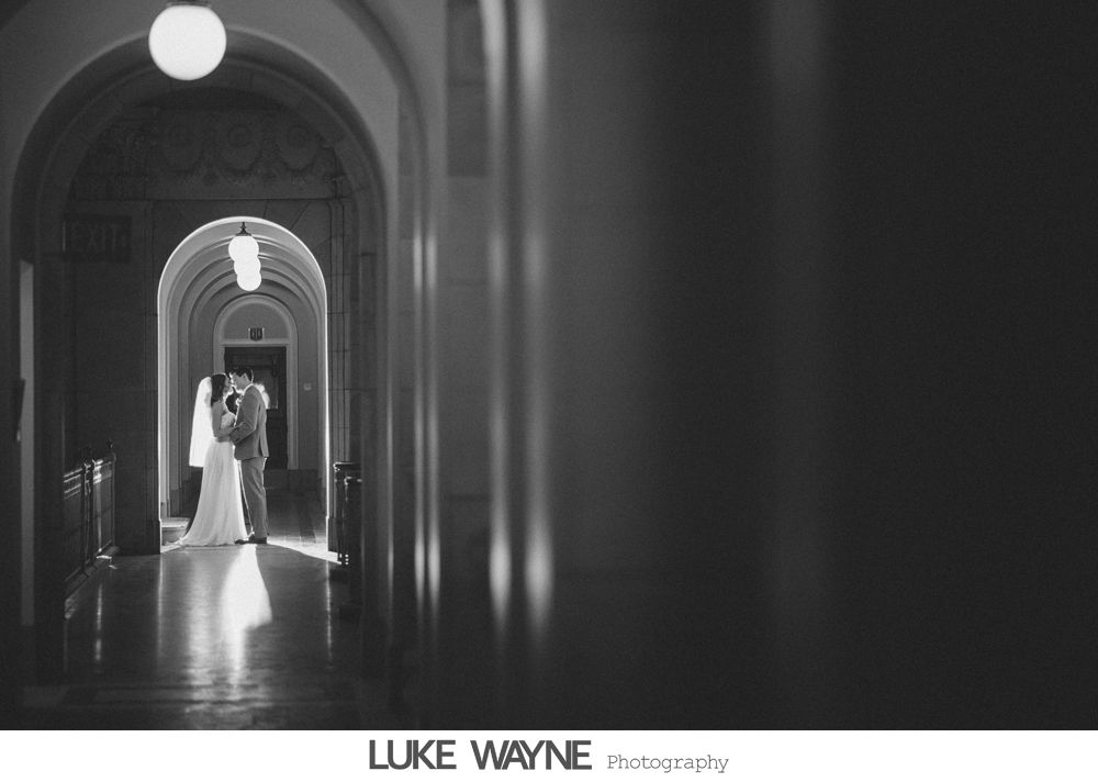 Bride in a fluffy white dress at a bar, smiling. Dark interior, fluorescent lights.