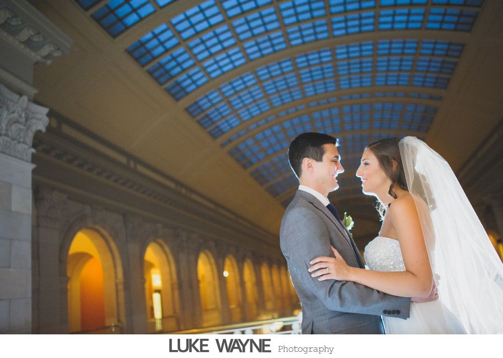 Bride and groom in wedding attire kissing in a dimly lit bar, next to a pool table.