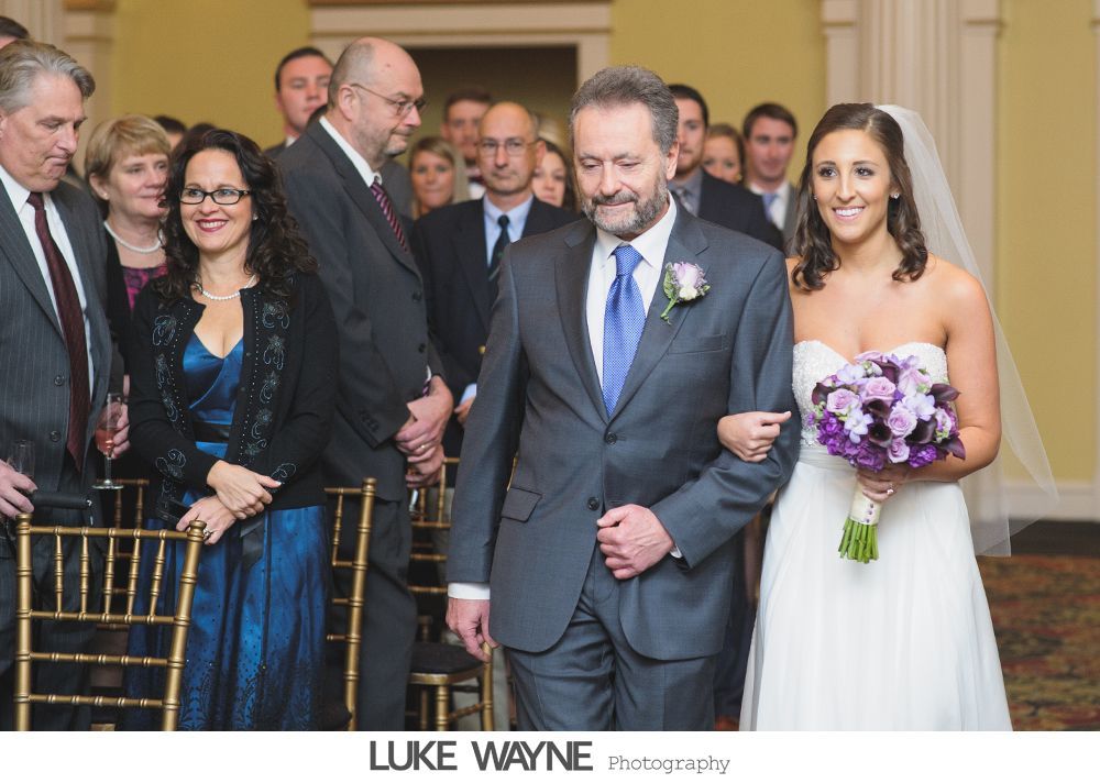 Couple in wedding attire embrace by open school bus door under a sunny sky.