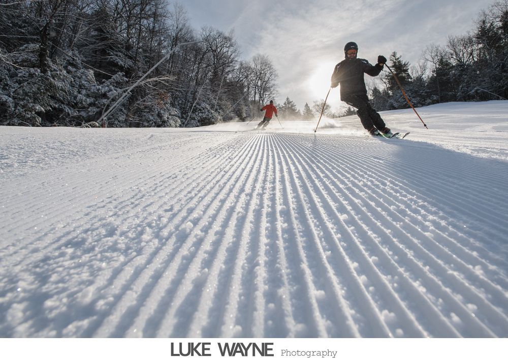 Silhouetted men helping each other with suits in a bright room by a window.