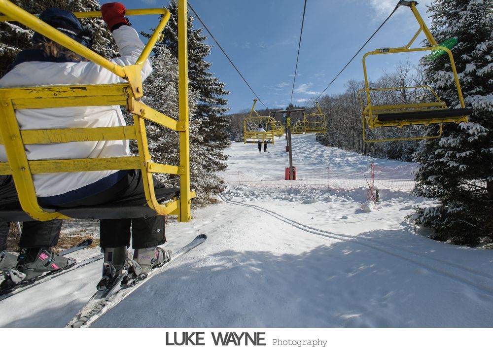 Two wedding dresses hanging in a window, with a chandelier and flowing fabric.