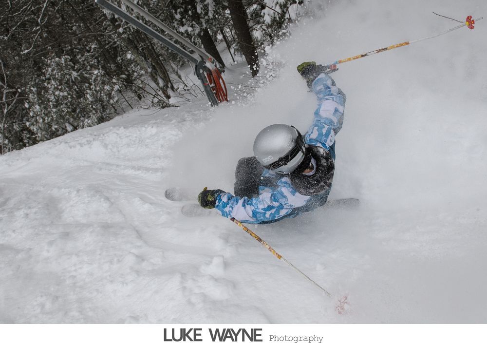 Wedding party toasting with champagne in a dimly lit bar, bride and groom center. Purple dresses, grey suits.