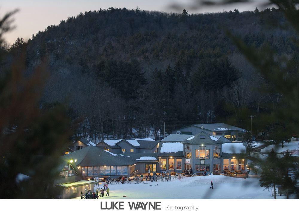 Bride and groom pose near dart boards. Bride in white dress, groom in suit. Indoor setting, red velvet ropes.