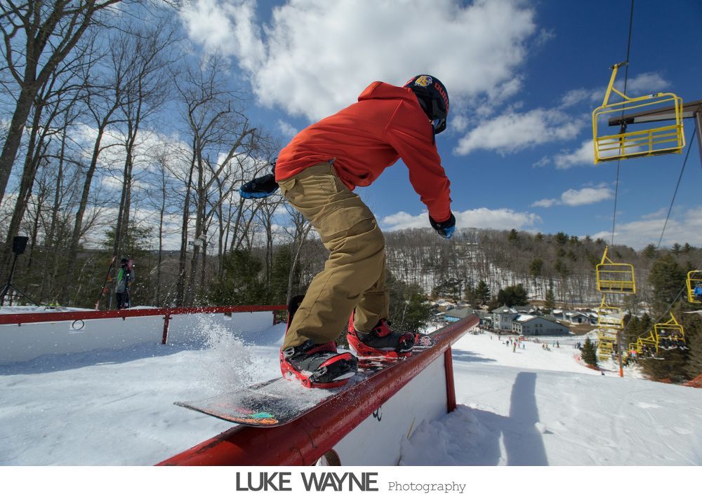 Bride and groom embrace, lit by spotlight, in front of a building with glowing windows at night.