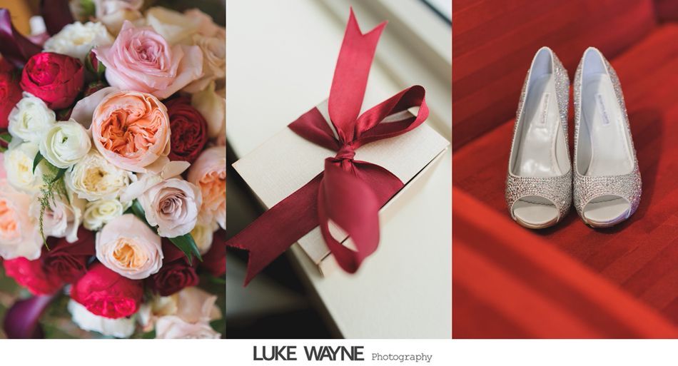 Bouquet of red, pink, and white flowers, gift box tied with maroon ribbon, and white heels on red surface.