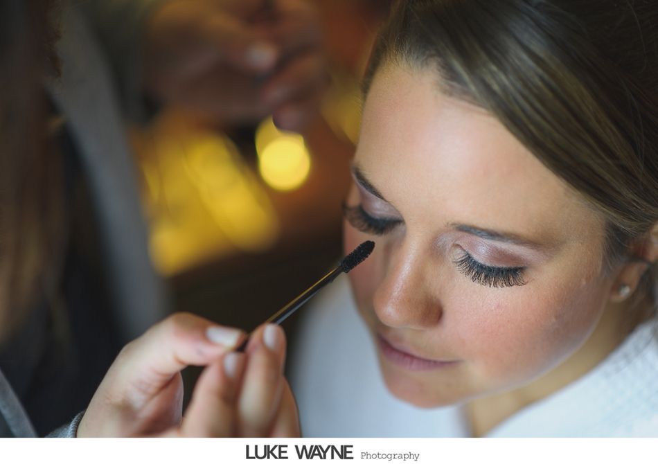 Woman having mascara applied, indoors. Soft lighting, makeup artist at work.