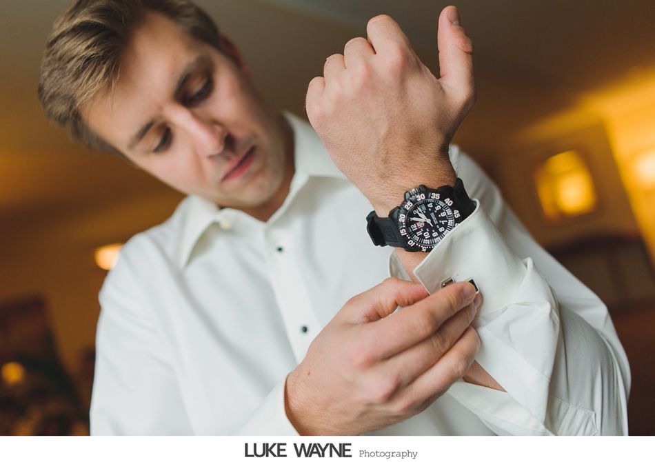 Man adjusting cufflink on white dress shirt, wearing black wristwatch. Indoor, soft light.
