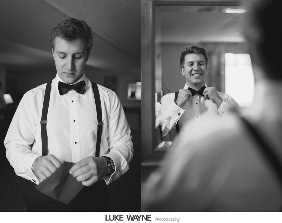 Groom in a tuxedo adjusting his bow tie in front of a mirror. Black and white.