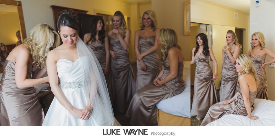 Bride in white gown surrounded by bridesmaids in brown dresses, adjusting her dress in a hotel room.