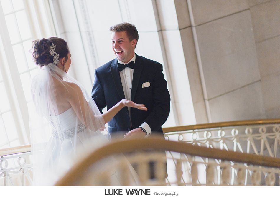 Bride and groom share a moment on a staircase. Bride gestures excitedly; groom smiles.