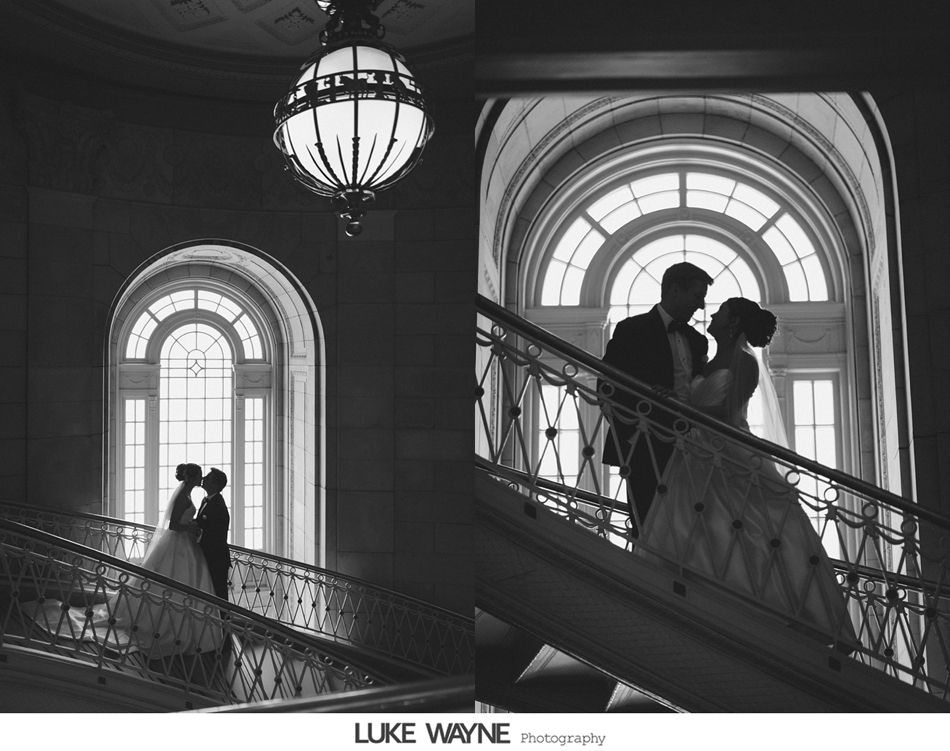 Couple on staircase kissing, silhouetted by large arched windows. Black and white photograph.