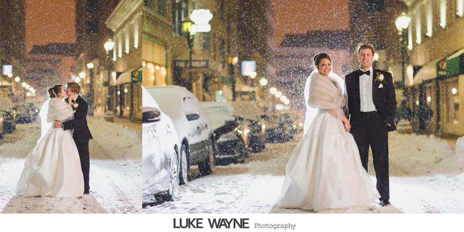 A newly married couple poses in the snowy street at night.