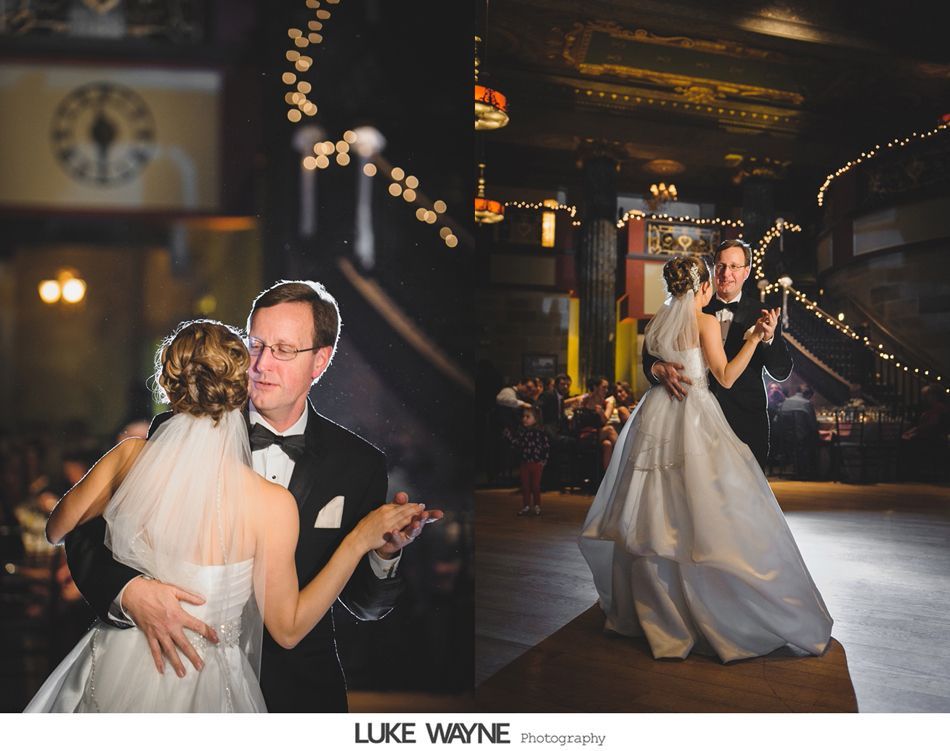Bride and father dance at a wedding reception. Dimly lit ballroom with string lights and stairs in the background.