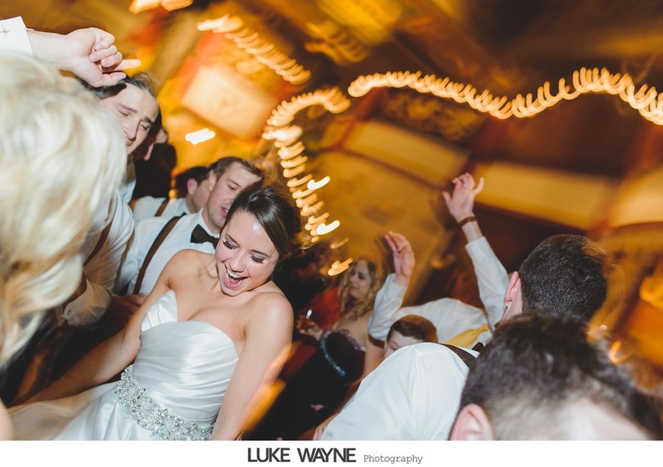 Bride dancing at a wedding reception, surrounded by guests. Soft focus, bright lights.