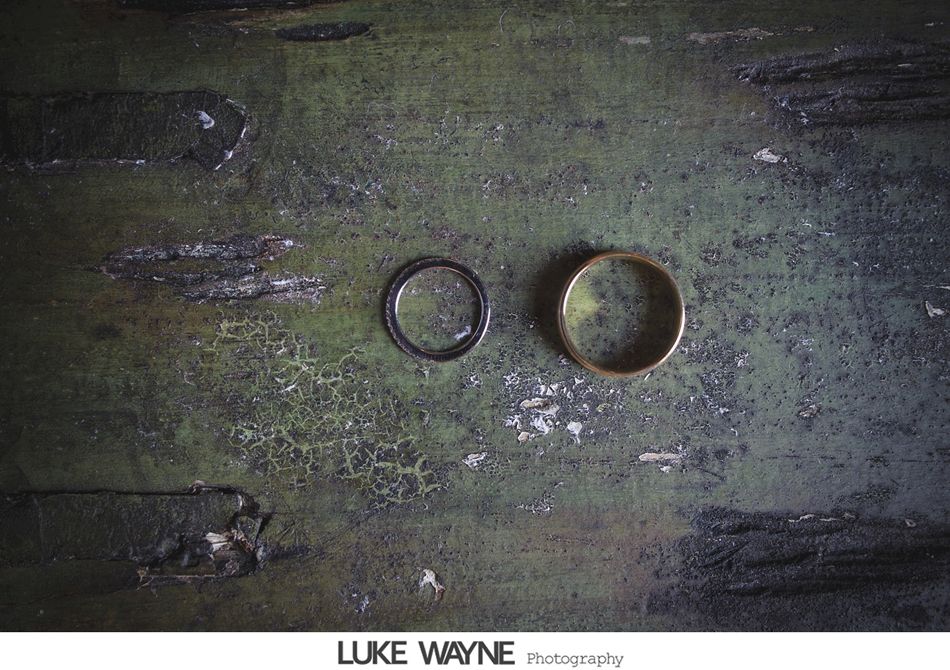 Two wedding rings, one silver, one gold, on a textured, weathered green surface.