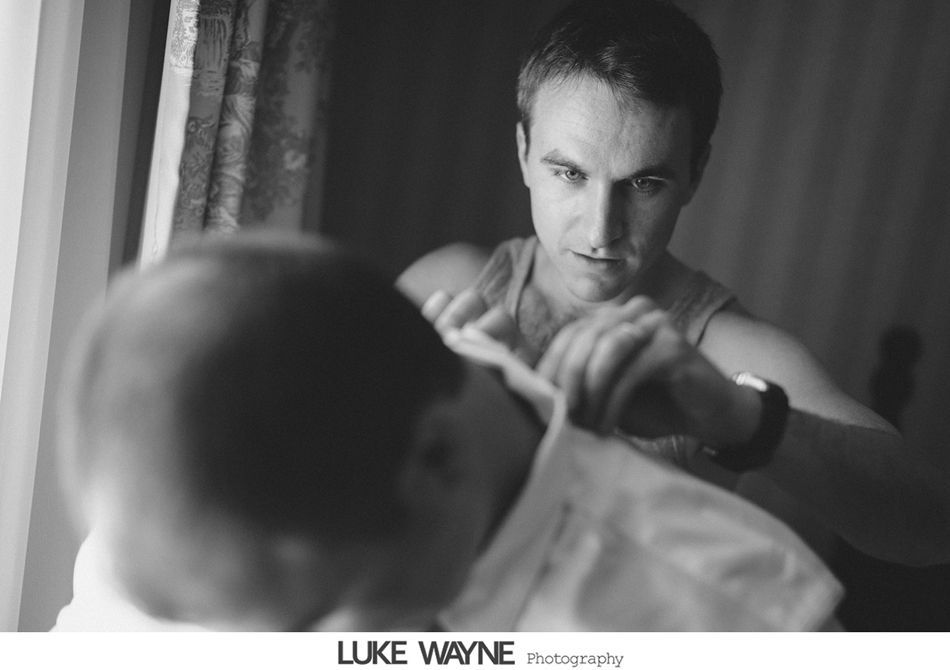 Man adjusting a shirt on a person; indoor, in front of a window.