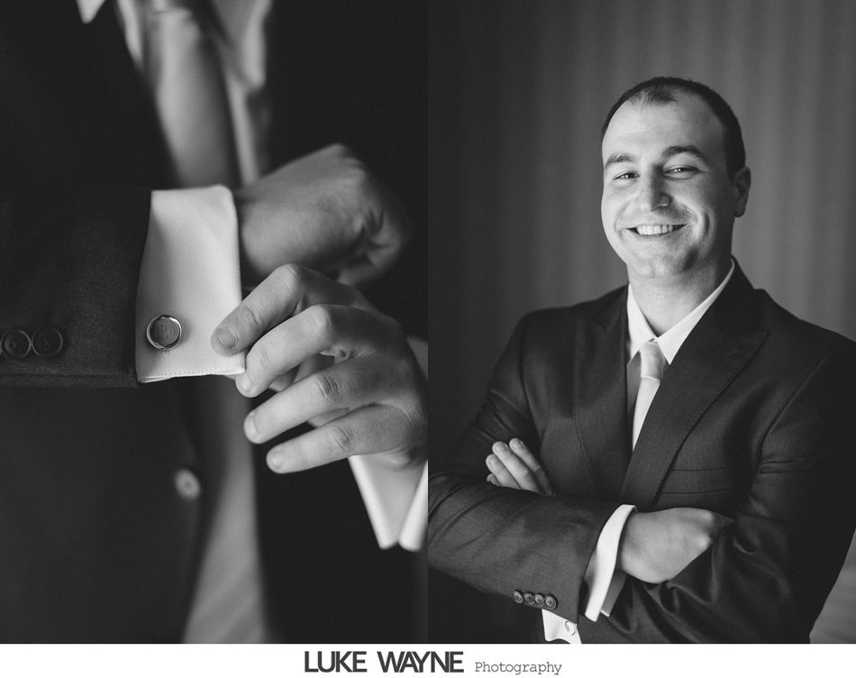 Man in suit adjusting cufflinks; smiling in formal portrait.
