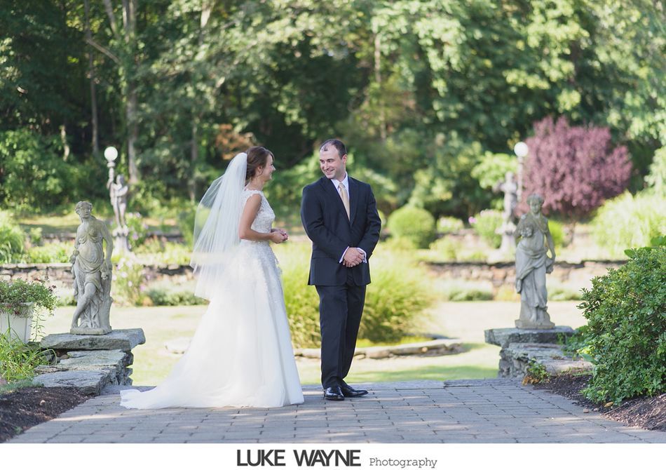 Bride and groom in a garden, facing each other. The bride wears a veil and gown, the groom a suit.