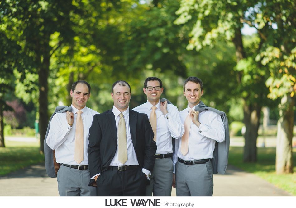 Four men in suits and ties pose outdoors, some holding jackets.