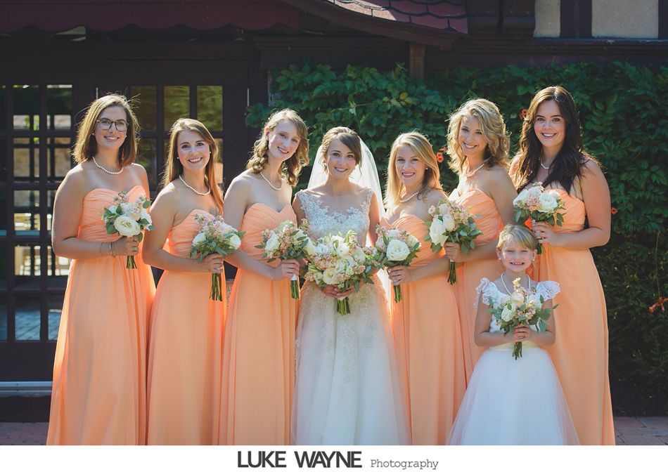 Bride and bridesmaids in peach dresses holding bouquets, posing outside a building.