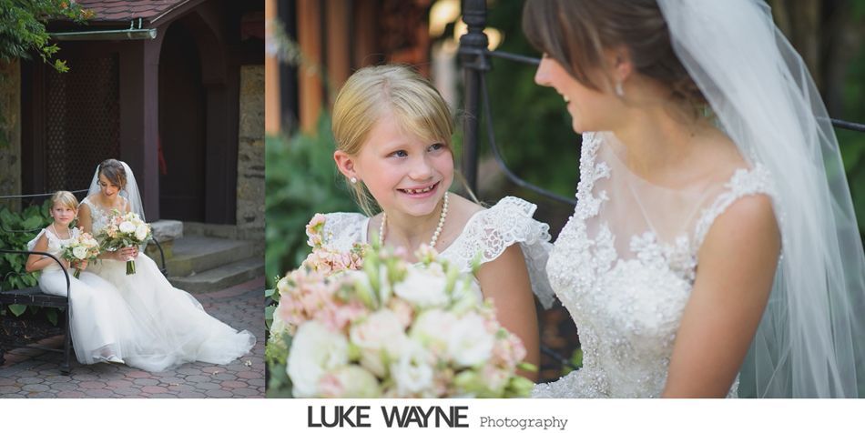 Bride smiles at flower girl outdoors. Both hold bouquets; white dresses.