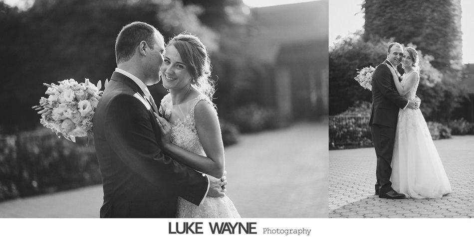 Newlyweds embrace, smiling, holding a bouquet. Black and white photo outside, likely at a wedding.