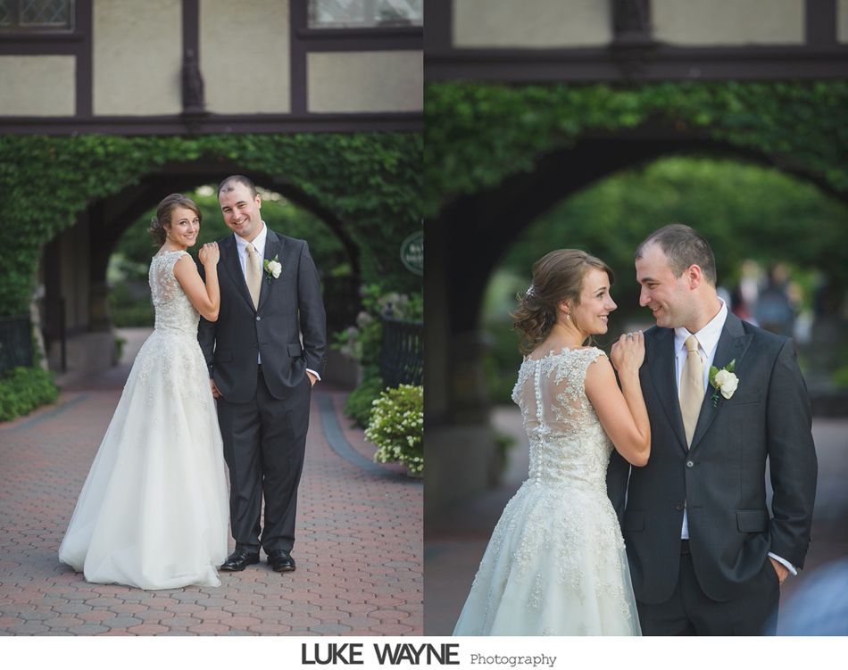 Bride and groom stand under ivy-covered archway. The bride wears a white gown, and the groom a dark suit.