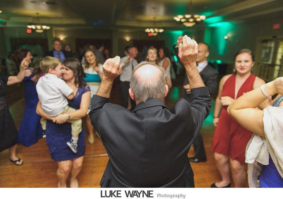 People dancing at an event, with a man raising arms. Green and warm lighting.