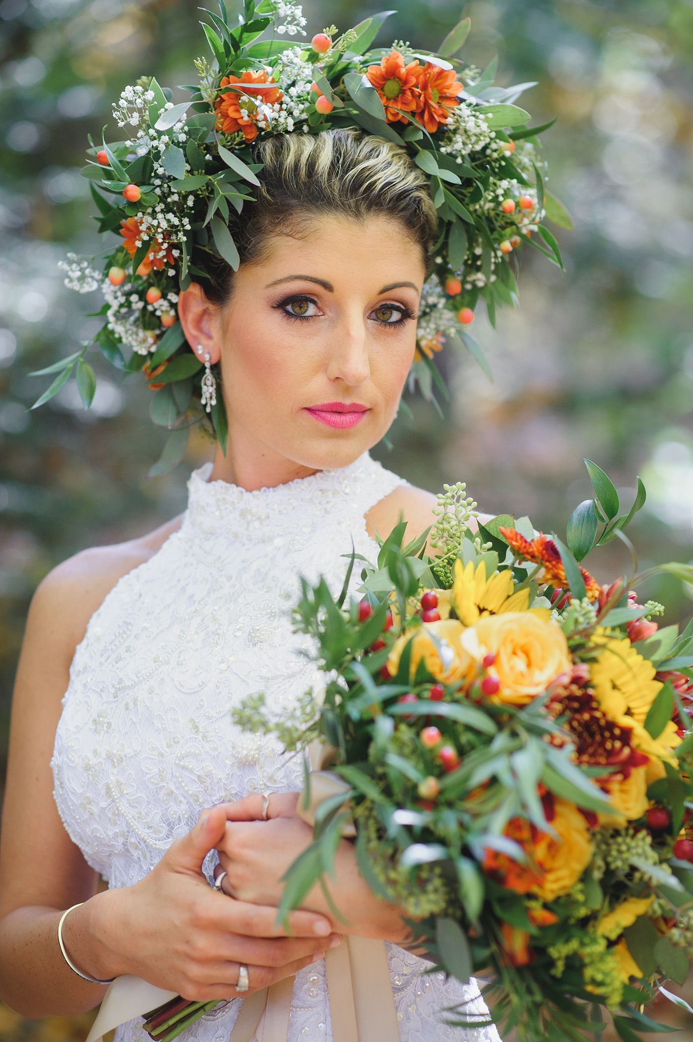 Bride in a white beaded dress and flower crown holding a bouquet, in an outdoor setting.