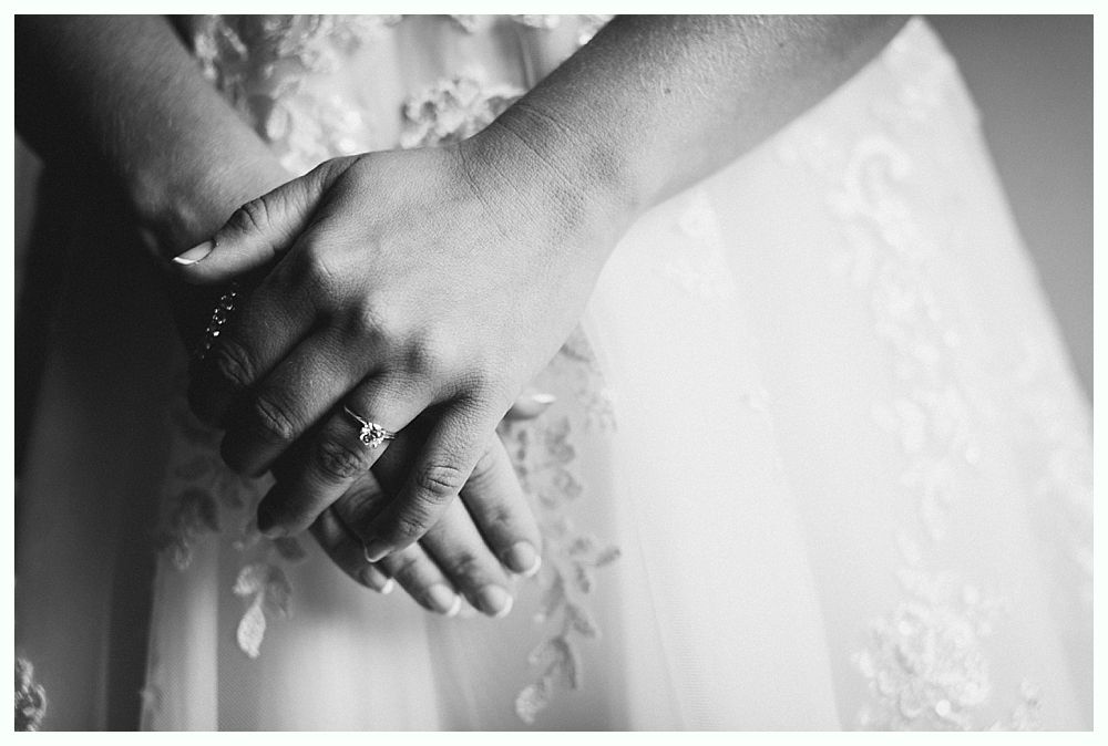 Hands clasped over a white wedding dress. A ring is visible on a finger.